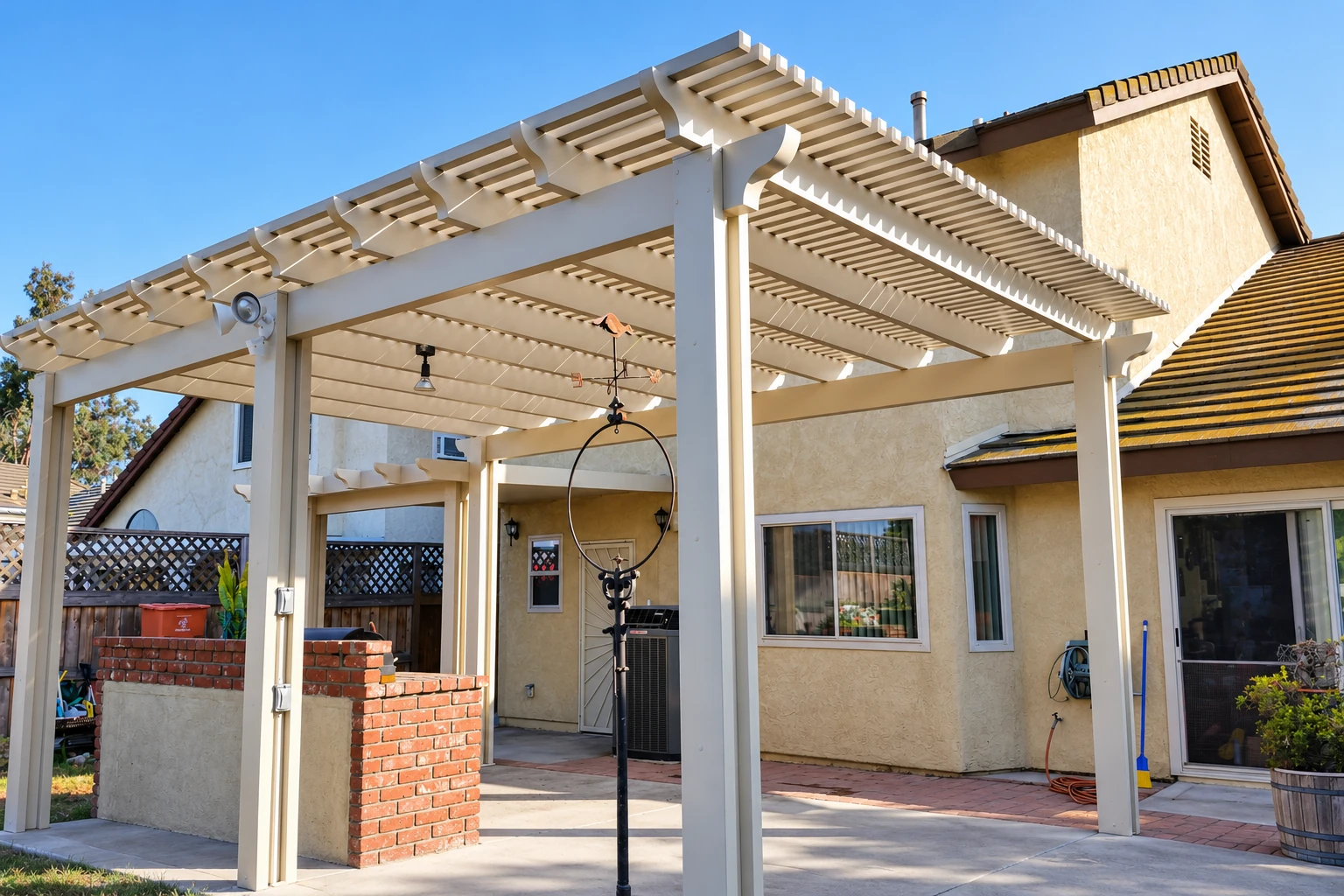 White pergola-style patio cover with slatted roof and sturdy posts beside a stucco house.